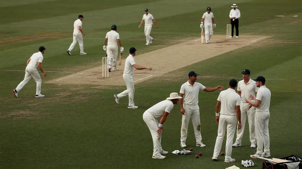 Medium view of fielders and a bowler adjusting positions on a professional cricket ground